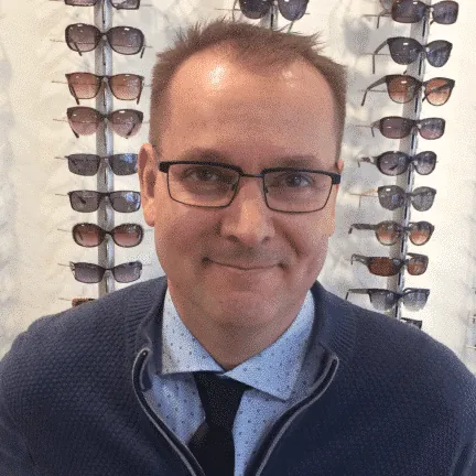 Ole Højer, the optician and optometrist at Ole Optica, smiling in front of a display of sunglasses